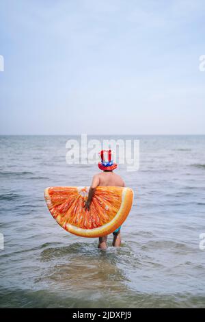 Homme transportant une tranche d'orange gonflable marchant dans la mer Banque D'Images