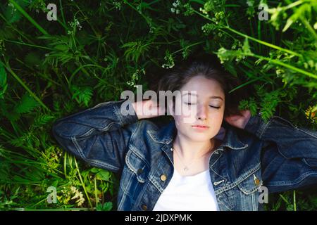 Une fille en veste denim se détendant avec les yeux fermés sur l'herbe Banque D'Images