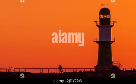 Rostock, Allemagne. 24th juin 2022. Un homme prend une photo du soleil levant sur la jetée de Warnemünde. Les météorologues s'attendent à de beaux temps d'été avec des températures allant jusqu'à 30 degrés dans les jours à venir. Credit: Jens Büttner/dpa/Alay Live News Banque D'Images