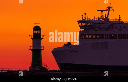 Rostock, Allemagne. 24th juin 2022. Le soleil levant colore le ciel au-dessus de la jetée du port de Warnemünde orange-rouge le matin. Le ferry « Copenhague » de la société de transport Scandilines quitte le port pour le Danemark. Les météorologistes s'attendent à des conditions météorologiques estivales très clémente avec des températures pouvant atteindre 30 degrés Celsius dans les jours à venir. Credit: Jens Büttner/dpa/Alay Live News Banque D'Images