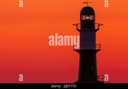 Rostock, Allemagne. 24th juin 2022. Le soleil levant colore le ciel au-dessus de la jetée du port de Warnemünde orange-rouge le matin. Les météorologues s'attendent à de beaux temps d'été avec des températures allant jusqu'à 30 degrés dans les jours à venir. Credit: Jens Büttner/dpa/Alay Live News Banque D'Images