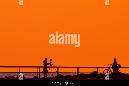 Rostock, Allemagne. 24th juin 2022. Un homme prend une photo du soleil levant sur la jetée de Warnemünde. Les météorologues s'attendent à de beaux temps d'été avec des températures allant jusqu'à 30 degrés dans les jours à venir. Credit: Jens Büttner/dpa/Alay Live News Banque D'Images