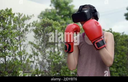 Une jeune femme porte un casque VR pour l'entraînement de boxe, un entraînement aérobie pour le boxe dans la réalité virtuelle dans le monde de la simulation. Banque D'Images