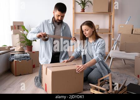 Homme et femme emballant le jour de déplacement. Guy scellant une boîte en carton avec du ruban adhésif, déplacement et concept de déplacement. Espace de copie. Banque D'Images