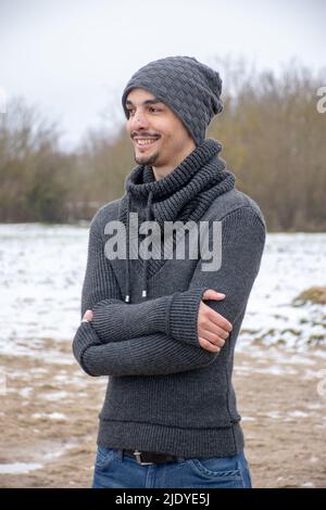 Un jeune homme se tient avec ses bras croisés par un lac. Il regarde la distance avec un sourire. Banque D'Images
