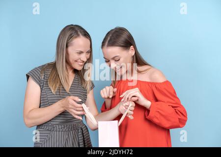 Vibrations shopping en famille. Portrait bonne mère et fille avec des sacs de shopping sur fond bleu dans des robes colorées. Fille se réjouit dans les achats à rabais et les cadeaux joyeusement gesticulate Banque D'Images