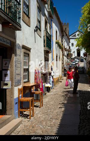 Les touristes parcourent les étals de souvenirs de Rua Direita à Óbidos, dans la région Centro du Portugal, en dessous de l'ancienne Igreja de Santiago ou São Tiago, l'ancienne église de Saint James datant de la fin du 18th siècle, qui abrite maintenant la librairie Livraria de Santiago. Banque D'Images