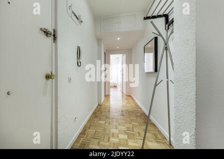 Hall d'entrée d'une maison avec un long hall au sol en chêne clair, des portes en bois blanc, un porte-manteau en métal et l'accès à plusieurs chambres Banque D'Images