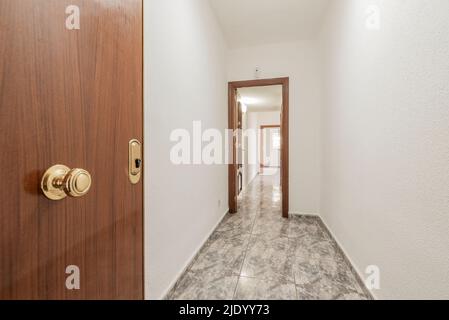 hall d'entrée allongé d'une maison avec porte en bois clair, sol carrelé en céramique grise et murs peints en gotelette blanche Banque D'Images