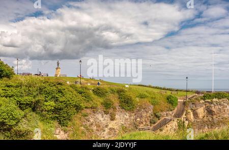 Des marches mènent au sommet d'une falaise avec une statue du capitaine Cook. Les gens s'assoient sur des bancs et un ciel nuageux est au-dessus. Banque D'Images
