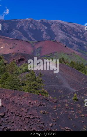 Sentier de randonnée circulaire autour de Monti Sartorius, pierres de lave rouges, sol volcanique, vue de bébé cratère, en arrière-plan volcan Etna, Sicile, Italie Banque D'Images