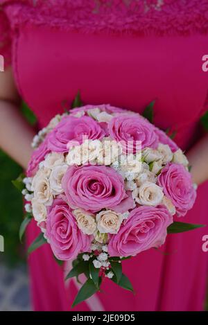 Gros plan d'une jeune femme portant une robe rose chaude tout en tenant un bouquet rond élégant avec de grandes roses assorties, jolie demoiselle d'honneur Banque D'Images