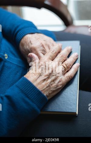 Les mains d'une femme plus âgée sur un livre fermé dans une attitude de repos et de détente. Banque D'Images