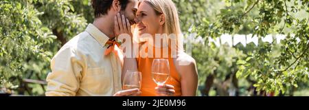 Vue latérale d'une femme gaie tenant un verre de vin et touchante petit ami dans le parc d'été, bannière Banque D'Images