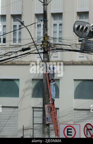 salvador, bahia, brésil - 20 juin 2022 : un homme sur une échelle met le câblage de teva sur un poteau électrique de réseau dans la ville de Salvador. Banque D'Images