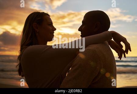 Un jeune couple interracial affectueux et affectueux se faisant face l'un à l'autre tout en passant du temps ensemble sur la plage au coucher du soleil. Amoureux du partage Banque D'Images