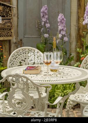 Bouteille de vin avec 2 verres et livre de poche sur une table de jardin en fonte blanche. Banque D'Images