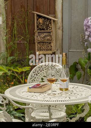 Bouteille de vin avec 2 verres et livre de poche sur une table de jardin en fonte blanche. Banque D'Images