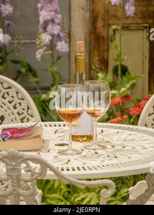 Bouteille de vin avec 2 verres et livre de poche sur une table de jardin en fonte blanche. Banque D'Images