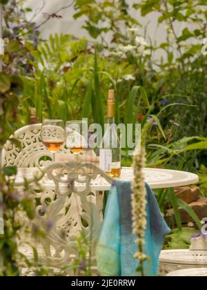 Bouteille de vin avec 2 verres et livre de poche sur une table de jardin en fonte blanche. Banque D'Images