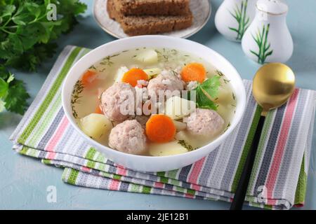 Soupe avec boulettes de poulet, riz et légumes dans un bol blanc sur fond bleu Banque D'Images