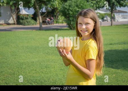 Bonne adolescente mangeant un hamburger dans le parc à l'extérieur. Banque D'Images