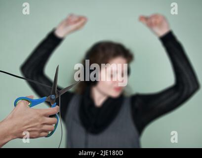 Arrêtez d'écouter de la musique ! Une main avec des ciseaux coupe le fil du casque à une fille dansante. Notion de censure, de limitation et d'interdiction Banque D'Images