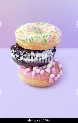 Pile de différents beignets sucrés et savoureux avec des saupoudrées sur une table mauve clair Banque D'Images