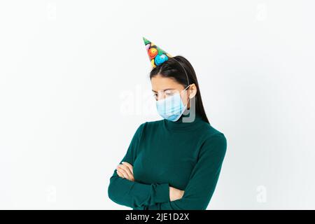 Fête d'anniversaire annulée en raison du virus covid, triste femme solitaire portant un masque et la casquette de partie se tient sur fond blanc studio, contrarié que la partie n Banque D'Images