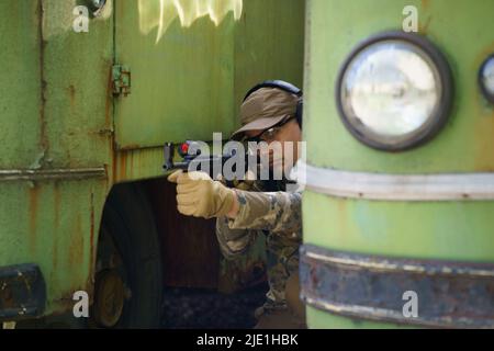 Entraînement aux troubles civils, l'homme en cours d'entraînement tactique se cache derrière les vieux véhicules rouillés. Formation de policiers à l'usine de tir avec arme. Cours d'entraînement tactique de l'homme de trooper commandé. Banque D'Images