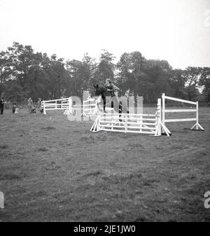 1940s, historique, une jeune fille à cheval sautant une clôture dans un champ, sans casque, Bramhall, Stockport, Angleterre, ROYAUME-UNI. Banque D'Images