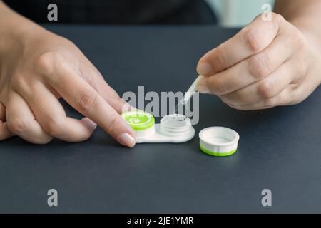 Fille sort la lentille de contact du conteneur avec une pince à épiler. Arrière-plan noir, gros plan, vue latérale Banque D'Images