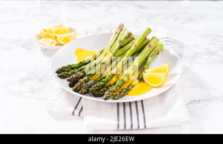 Sert des asperges cuites à la vapeur avec une sauce hollandaise maison et des quartiers de citron sur une assiette blanche. Banque D'Images