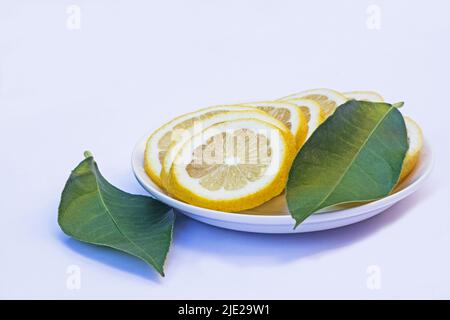 Tranches de citrons et de feuilles vertes sur une plaque blanche isolée sur fond blanc Banque D'Images