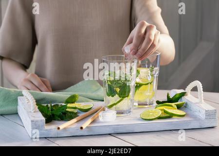 Une fille prépare des cocktails rafraîchissants de fruits mojito avec de la chaux et de la menthe. Banque D'Images