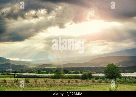 Coucher de soleil dans les Alpes françaises. Paysage de campagne en Provence avec jardins de pommiers, collines et ciel nuageux Banque D'Images