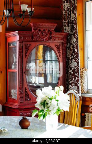 Intérieur rural de la cuisine avec bouquet de fleurs de lilas blanc dans un vase sur une table et armoire rouge vintage dans une maison en bois. Banque D'Images