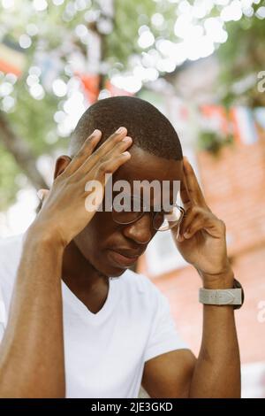 Vertical de l'homme épuisé, stressé multiracial foncé peau dans les lunettes en gardant les mains sur la tête, la souffrance, en vissant les yeux Banque D'Images