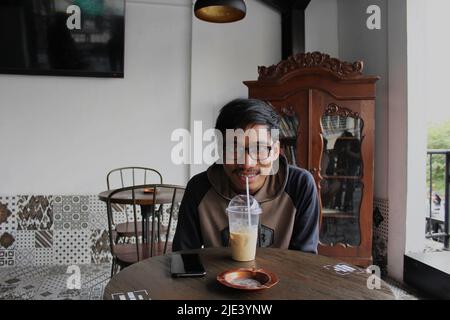 Yogyakarta, Indonésie - 08 07 2019: Une expression heureuse d'un homme qui profite d'un verre de café froid pendant ses vacances à Yogyakarta, dans le centre de Java Banque D'Images