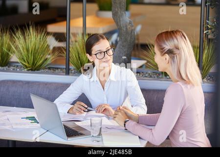 Des jeunes femmes d'affaires intéressantes et positives sont présentes dans un restaurant écologique et consultent les données analytiques tout en remue-méninges sur la mise en œuvre du projet Banque D'Images