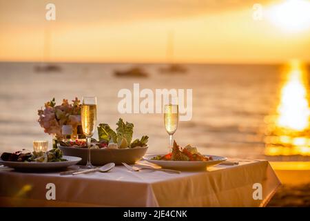 Dîner romantique au coucher du soleil sur la plage. Table pour deux avec cuisine de luxe, verres de champagne dans un restaurant avec vue sur la mer. L'amour de l'été Banque D'Images