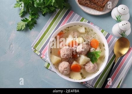 Soupe avec boulettes de poulet, riz et légumes dans un bol blanc sur fond bleu, vue du dessus Banque D'Images