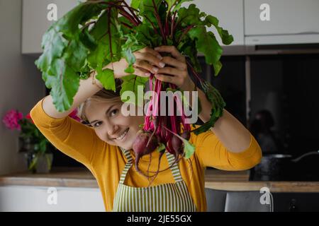 Femme blonde souriante tenant un bouquet de betteraves, cuisant de la salade saine biologique fraîche dans la cuisine en été. Nourriture écologique Banque D'Images