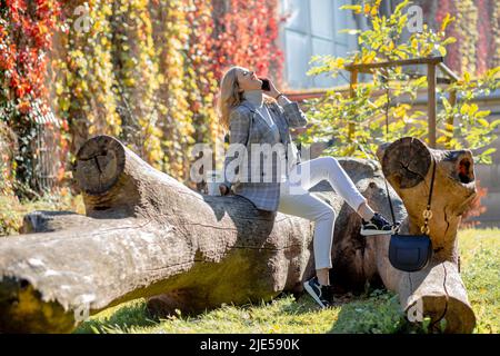 Belle femme riant inlassablement avec sa tête projetée sur le soleil jour d'automne, assis sur un grand arbre tombé dans le parc d'automne. Émotions positives Banque D'Images