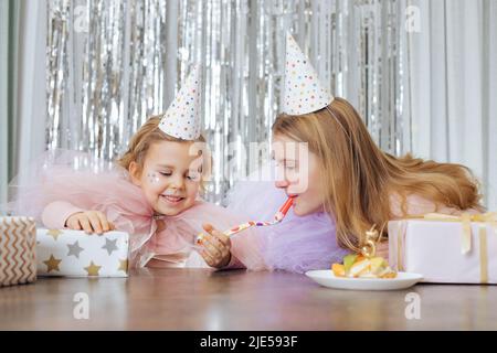 Moments drôles de célébrer l'anniversaire de la fille de 5 ans. Deux sœurs en chapeaux de fête sont heureux ensemble entouré de cadeaux et de gâteau avec numéro de bougie Banque D'Images