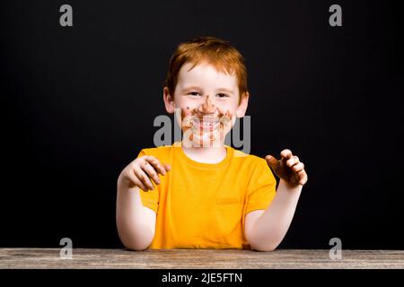 l'enfant dans les mains a fondu le chocolat et le garçon a tous souillé dans la fonte du chocolat au lait avec du sucre Banque D'Images