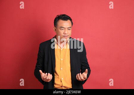 L'homme asiatique d'âge moyen debout sur fond rouge. Banque D'Images