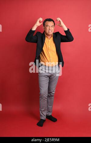 L'homme asiatique d'âge moyen debout sur fond rouge. Banque D'Images