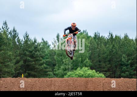 Dobele, Lettonie, 18 juin 2022: Le coureur de motocross en vol, saute et déchaîne sur un tremplin contre le ciel Banque D'Images