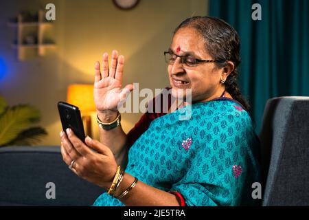 Les vieilles femmes qui font des appels vidéo sur téléphone mobile tout en étant assis sur le canapé à la maison - concepts de technologie, de détente et de plaisir. Banque D'Images